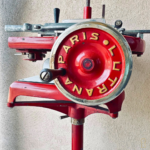 Ancienne machine à trancher Lutrana Paris sur pied en métal rouge, objet vintage de boucherie et décoration industrielle.